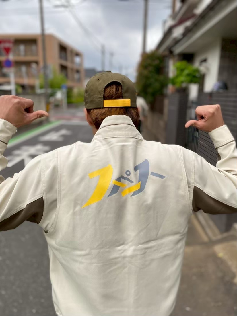 会社のユニフォームを着て背中を向けている。背中にはスペースのロゴが大きくついている。